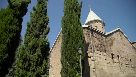 A-low-angle-view-over-the-trees-of-the-12th-century-Georgian-Orthodox-church-in-the-Lurji-Monastery,-or-"Blue-Church",-in-Tbilisi-Georgia