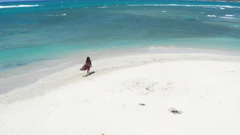 Aerial-dolly-forward-towards-woman-tourist-in-bikini-on-white-sand-beach-waves-washing-ashore