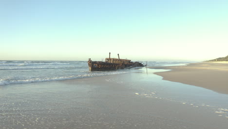 Drone-approaching-the-old-shipwreck,-SS-Maheno,-on-a-beautiful-beach-of-Fraser-Island,-Australia