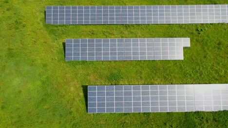 Solar-panel-park,-an-aerial-drone-view-of-multiple-solar-panels-lined-up-in-a-rural-green-field-top-down-view