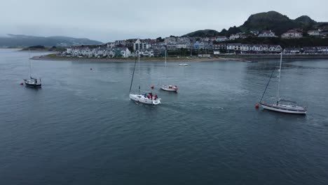 Aerial-follow-view-behind-yacht-navigating-seaside-mountain-Welsh-town-quiet-river-Conwy-estuary
