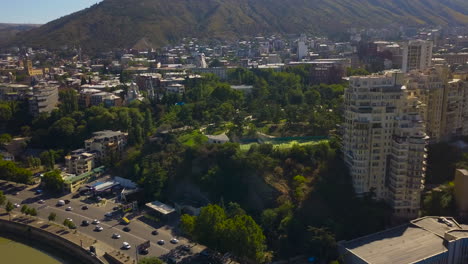 A-busy-highway-with-a-beautiful-city-near-the-mountains-view-by-drone-flight,-Tbilisi,-Georgia