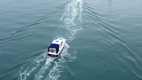 Luftaufnahme-über-Dem-Motorboot,-Das-Die-Flussmündung-Zwischen-Verankerten-Segelschiffen-Verlässt