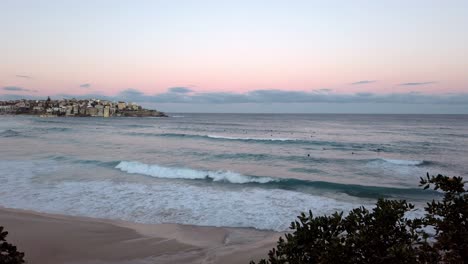 Brechende-Wellen-Ans-Ufer-Mit-Surfern-Am-Bondi-Beach-Bei-Sonnenuntergang-In-Sydney,-Nsw-Australien