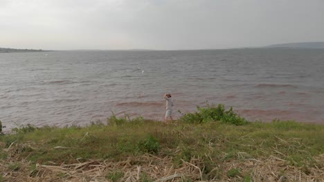A-man-dressed-in-a-safari-suit-looking-out-at-Lake-Victoria-in-rural-Africa