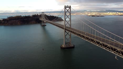 4K-30fps-Aerial-Drone-Footage-of-San-Francisco-Oakland-Bay-Bridge,-Yerba-Buena-Island---Cars-Travel-on-Highway,-Stormy-Clouds,-Calm-Bay-Water,-Sunset-Reflecting-off-Waves,-World-Record-Architecture