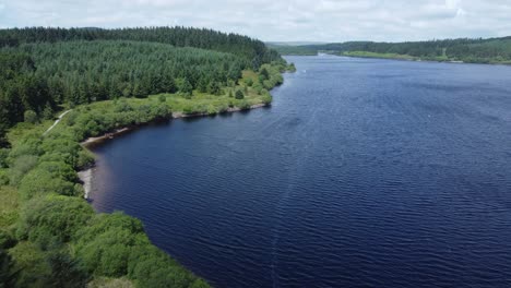 Idyllic-blue-water-reservoir-lake-woodland-hiking-walk-aerial-view-slow-forward-push-in