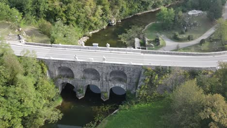 An-aerial-view-over-road-and-stone-arched-bridge-in-Tounj,-Croatia-in-late-summer