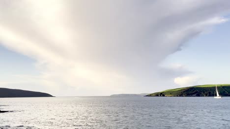 Einsames-Segelboot-Beim-Verlassen-Der-Sicherheit-Des-Hafens-In-Kinsale,-Irland-Mit-Dramatischer-Wolke-über-Blauem-Himmel