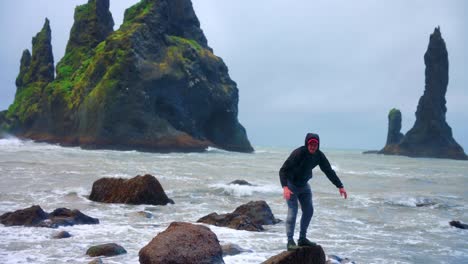 Tourist-Stands-At-The-Small-Rock-At-Reynisfjara-Beach-In-Iceland-With-The-Reynisdrangar-At-The-Background