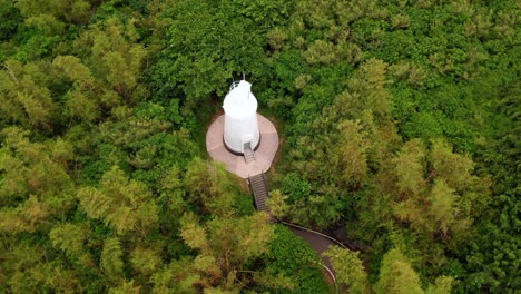Kreisförmige-Luftpfanne,-Die-Den-Weißen-Leuchtturmturm-Auf-Dem-Hügel-Einfängt,-Der-Lichtstrahlen-Aussendet,-Um-Die-Sicherheit-Der-Boote-Auf-See-Zu-Gewährleisten,-Umgeben-Von-Grünem-Wald-Auf-Der-Insel-Xiaoliuqiu-Lambai