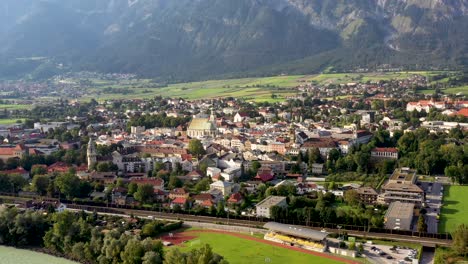 Aerial-shot-of-mountain-town-of-Austria-with-churches,colorful-houses,-tower,-autumn-scenery-at-sunset,-river-Austrian-Alps-from-above,-Austria,-Europe
