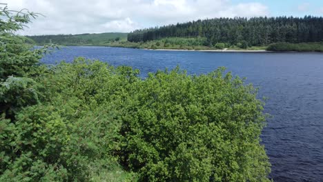 Idyllic-blue-water-reservoir-lake-woodland-hiking-walk-aerial-view-close-to-shoreline-trees