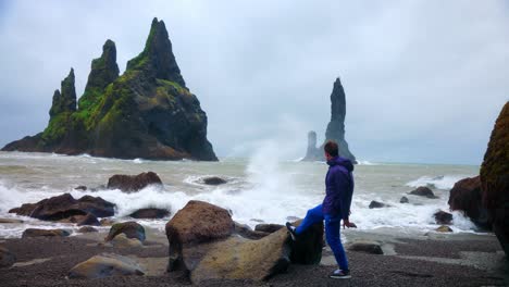 Man-Looking-At-The-Reynisdrangar-Sea-Stacks-And-The-Strong-Waves-Of-Reynisfjara-Beach-In-South-Iceland