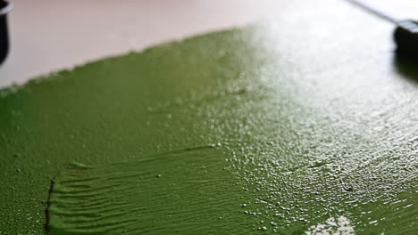 View-Of-Man-Applying-Green-Paint-To-A-Tabletop-During-Daytime---close-up