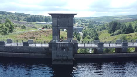 Alwen-reservoir-Welsh-woodland-shimmering-lake-water-supply-aerial-view-concrete-dam-countryside-park-pull-back-low