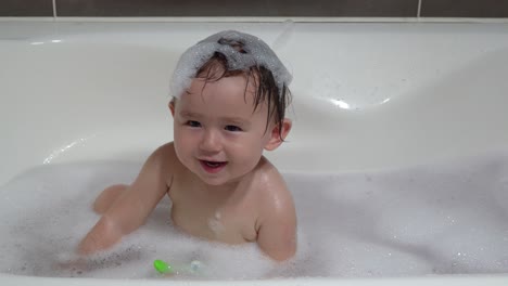 Little-MIxed-Ethnithity-One-year-old-Baby-Girl-Enjoying-Taking-Bath-with-Foam-Happily-Showing-Toothy-Smile-while-Having-Foam-on-Wet-Hair-in-Bathtub-at-Home