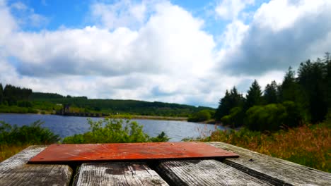 Low-angle-wooden-plank-picnic-table-overlooking-blue-sky-scenic-reservoir-lake-landscape-dolly-left
