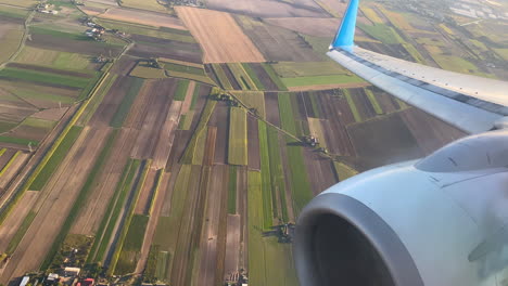 Close-up-shot-of-turbine-of-airplane-and-rural-colorful-farm-fields-in-with-differenet-pattern-during-landing-approach