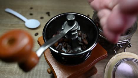 Left-hand-taking-coffee-beans-from-the-jar-and-fills-the-grinder-while-some-beans-fall-on-the-table