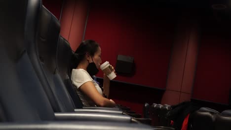 Seitenansicht-Einer-Einsamen-Dame,-Die-Kaffee-Trinkt,-Während-Sie-Allein-In-Einem-Leeren-Kino-Sitzt