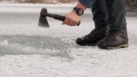 Fisherman-breaking-ice-with-an-axe-on-a-frozen-lake-in-winter
