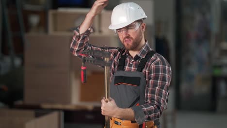 angry-young-man-in-work-uniform-beats-himself-with-a-tool-on-the-helmet