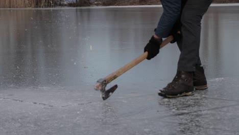 Person-breaking-ice-of-a-frozen-lake-in-winter