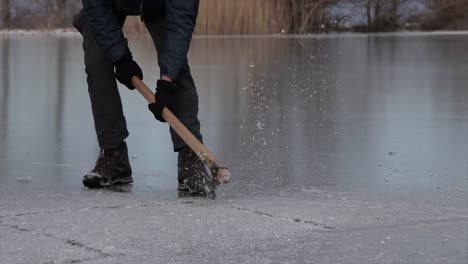 Person-breaking-ice-of-a-frozen-lake-with-an-axe