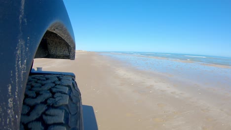 Right-front-tire-of-vehicle-driving-on-a-beach-on-a-sunny-day-on-South-Padre-Island-Texas--Point-of-view,-POV