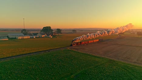 Aerial-View-of-a-Steam-Engine-with-Passenger-Cars-at-the-Golden-Sunrise-Approaching-with-a-Full-Head-of-Steam-and-Smoke-traveling-Thru-the-Farmlands