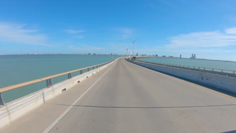 POV-thru-rear-window-while-driving-up-the-bridge-on-Queen-Isabella-Causeway-over-the-shipping-lane-on-the-Laguna-Madre-at-South-Padre-Island,-Texas