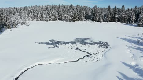Snow-covered-frozen-lake-in-winter,-Crno-jezero-or-Black-Lake-on-Pohorje-near-Rogla-ski-resor-from-the-air,-winter-wonderland-with-snowapped-treetops