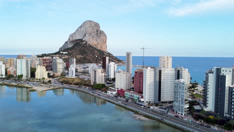 Vertical-booming-aerial-record-of-Lake-Les-Salines-in-the-foreground-and-the-Penyal-d'Ifac-Natural-Park-in-Calp,-Alicante,-Spain