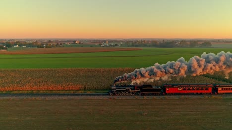 Aerial-View-of-a-Steam-Engine-and-Passenger-Cars-at-the-Golden-Sunrise-with-a-Full-Head-of-Steam-and-Smoke-Traveling-Thru-the-Farmlands