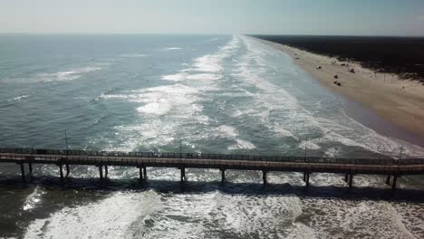 Drone-aerial-view-of-long-pier,-people-on-the-beach,-dunes,-and-waves-at-Nueces-County-Coastal-Park-on-North-Padre-Island,-Texas