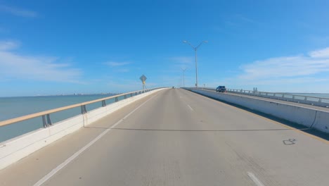 POV-thru-rear-window-while-driving-over-Queen-Isabella-Causeway-over-Laguna-Madre-at-South-Padre-Island,-Texas-on-a-sunny-afternoon