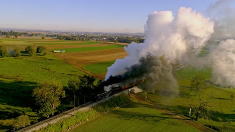 Aerial-View-of-Farmlands-at-Sunrise-with-a-Steam-Engine-and-Passenger-Train-Approaching-with-a-Full-Head-of-Steam-and-Smoke