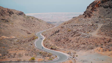 Static-wide-shot-of-car-driving-on-curvy-road-between-rocky-mountain-of-Gran-Canaria