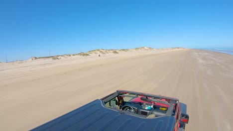 POV-from-roof-top-while-driving-on-a-nearly-deserted-beach-of-a-barrier-island-on-the-gulf-of-Mexico,-driver-waves-his-arms---Texas