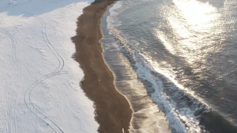 Midday-sunlight-shines-bright-on-Sandvik-beach-covered-in-snow-with-waves