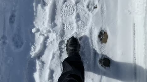 Person-Mit-Schwarzen-Stiefeln,-Die-An-Einem-Sonnigen-Tag-Auf-Einem-Schneebedeckten-Bürgersteig-Spazieren-Gehen