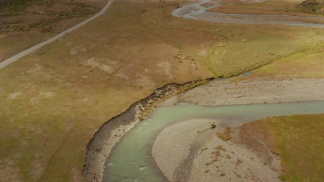 Aerial-tilt-up-shot-of-a-winding-river-in-a-dry-grassland-near-big-mountains-in-New-Zealand
