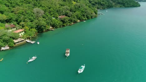 Aerial-drone-fly-by-boats-near-a-coast-of-an-island-with-lots-of-vegetation-and-green-tropical-forest