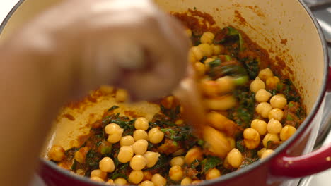 Dumping-chickpeas-into-a-red-paste-or-sauce-simmering-in-the-pot-on-the-stove-then-mixing