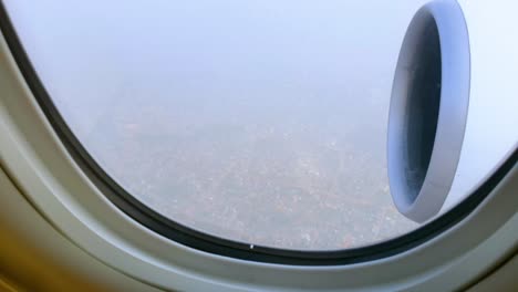 View-through-airplane-window-over-the-city-during-landing-on-cloudy-day