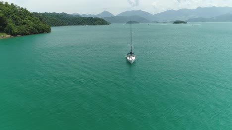 Aerial-drone-shot-of-sail-boat-arriving-to-a-beautiful-tropical-island-with-native-brazilian-vegetation-and-desert-beach