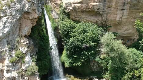 Aerial-views-of-a-waterfall-with-a-cave-and-an-old-building-in-Catalonia,-Spain