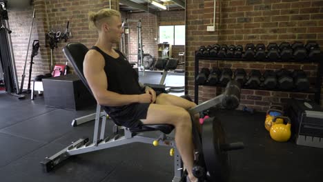 Tattooed-man-in-home-gym-sitting-on-chair-doing-quad-extension