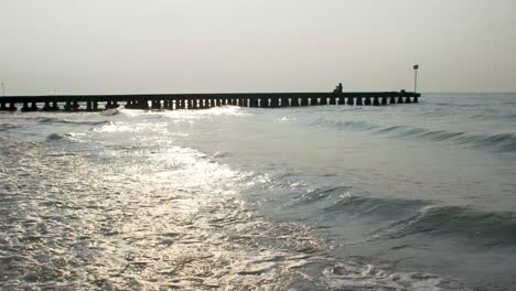 Small-waves-on-a-sandy-beach-with-a-jetty-and-blue-sky-with-sun-is-shining